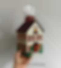 A hand holds a handkerchief dispenser in the shape of a crocheted house.