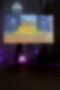 Exhibition view in the church: In the middle of the room is a screen showing a video work. People are standing in front of the screen, golden glitter is lying on the floor.