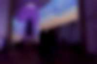 Ausstellungsansicht in der Kirche: Im Kirchenraum, der in ein violettes Licht getaucht ist, stehen Personen und schauen sich eine Videoarbeit auf einer großen Leinwand an.
