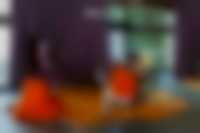 Ausstellungsansicht im Neubau: 2 Personen auf einer Bank und eine Person auf einem orangenen Sitzsack schauen sich eine Videoarbeit an.